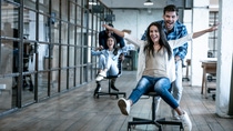 Work hard play hard. Four young cheerful business people in smart casual wear having fun while racing on office chairs and smiling.