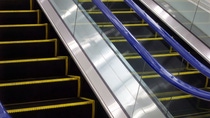 Escalator with black steps and yellow safety edges between glass side panels.
