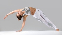 Young attractive woman practicing yoga, stretching in Bending Side Plank exercise, Vasisthasana pose, working out wearing sportswear, indoor full length, isolated against grey studio background
