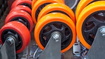 Polyurethane caster wheels in red and orange mounted on metal brackets for industrial material handling. Polyurethane caster wheels in red and orange mounted on metal brackets for industrial material handling.