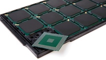 Semiconductor chip placed in front of a tray containing multiple integrated circuits.