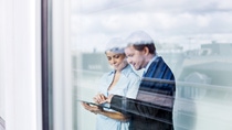 Business people standing behind glass wall using tablet computer Business people standing behind glass wall using tablet computer