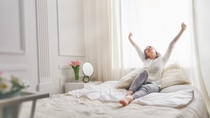 Happy young woman enjoying sunny morning on the bed