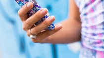 Female Hands holding smartphone. Young tanned  woman holding mobile phone,checking news and typing sms, wearing blue dress and ring.Mobile in bright cover.