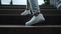 Person wearing white sneakers and light gray pants climbing brown stone stairs — capturing movement, casual style, and outdoor urban design.