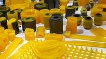 Assorted yellow polyurethane and rubber components displayed together, including bushings, rollers, and molded parts. Assorted yellow polyurethane and rubber components displayed together, including bushings, rollers, and molded parts.