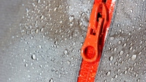 Orange zipper on a water-resistant fabric surface covered with water droplets.