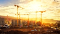 Large construction site including several cranes working on a building complex, illumined by warm gold sunlight