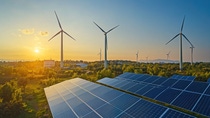 Large-scale solar panels and onshore wind turbines generate renewable energy in a natural landscape at sunrise.