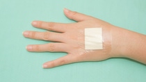 Adhesive bandage secured on the back of a hand with transparent medical tape.