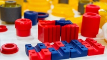 Red and blue polyurethane wear parts and bushings displayed with other molded industrial components. Red and blue polyurethane wear parts and bushings displayed with other molded industrial components.