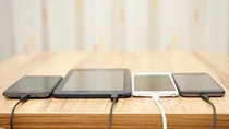 Smartphones and tablets connected to charging cables on a wooden table.
