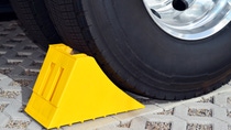 Yellow wheel chock positioned against a vehicle tire to prevent rolling. Yellow wheel chock positioned against a vehicle tire to prevent rolling.