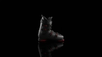 Black ski boot with red accents on a reflective surface against a black background. 

