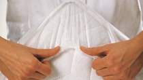 Hands stretching a transparent nonwoven medical fabric or protective material to show flexibility.