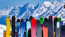 Colorful skis lined up in the snow with snow-covered mountains in the background. 
