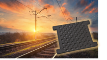Railway tracks at sunrise with a textured black rail pad displayed in the foreground.