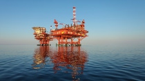 Offshore oil and gas platform standing in calm ocean waters, reflected on the sea surface.