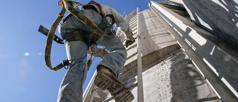 An Oilfield Worker Climbs a Ladder on the Side of a Mud Tank at an Oil and Gas Drilling Pad Site on a Sunny Morning
