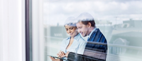 Business people standing behind glass wall using tablet computer Business people standing behind glass wall using tablet computer