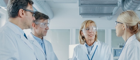 two men and two women scientists wearing safety goggles having a discussing  