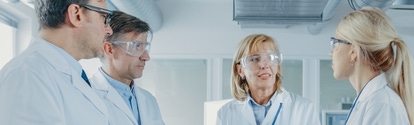 two men and two women scientists wearing safety goggles having a discussing  