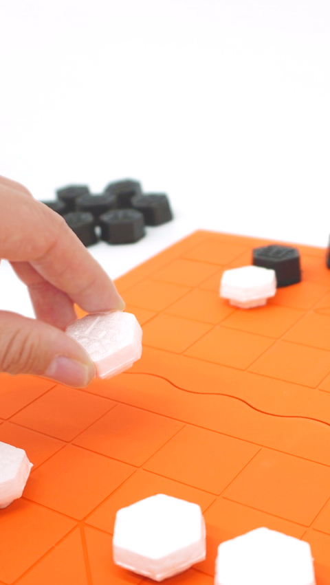 A player moves a Xiangqi piece on the orange game board, demonstrating the use of the custom game set made from BASF materials.