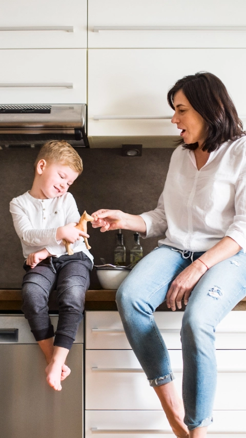 Happy senior woman with a small boy in the kitchen at home, relaxing.