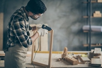 Profile side photo of serious concentrated worker man use electric hot glue gun to repair wooden construction frame work in home house garage Profile side photo of serious concentrated worker man use electric hot glue gun to repair wooden construction frame work in home house garage