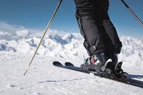 Skier standing on skis in snow, viewed from behind, with ski poles and snow-covered mountains in the background. 
