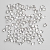 Transparent plastic pellets scattered on a light gray surface, shown as a raw material sample.
