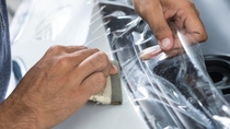 Hands applying a transparent protective film to a vehicle surface.
