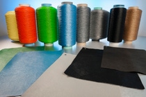 Spools of colored industrial fibers and nonwoven material samples displayed on a tabletop. 