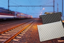 Vías ferroviarias en una estación con trenes en movimiento; placas elastoméricas texturizadas negras y blancas en primer plano. Vías ferroviarias en una estación con trenes en movimiento; placas elastoméricas texturizadas negras y blancas en primer plano.