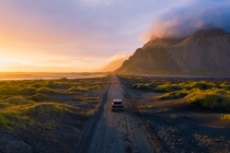 Gravel road at a golden Sunset with Vestrahorn mountain in the background and a car driving the road in Iceland Gravel road at a golden Sunset with Vestrahorn mountain in the background and a car driving the road in Iceland