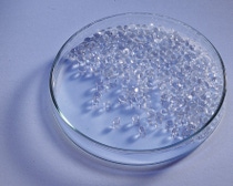 Transparent plastic pellets in a glass petri dish on a light background.